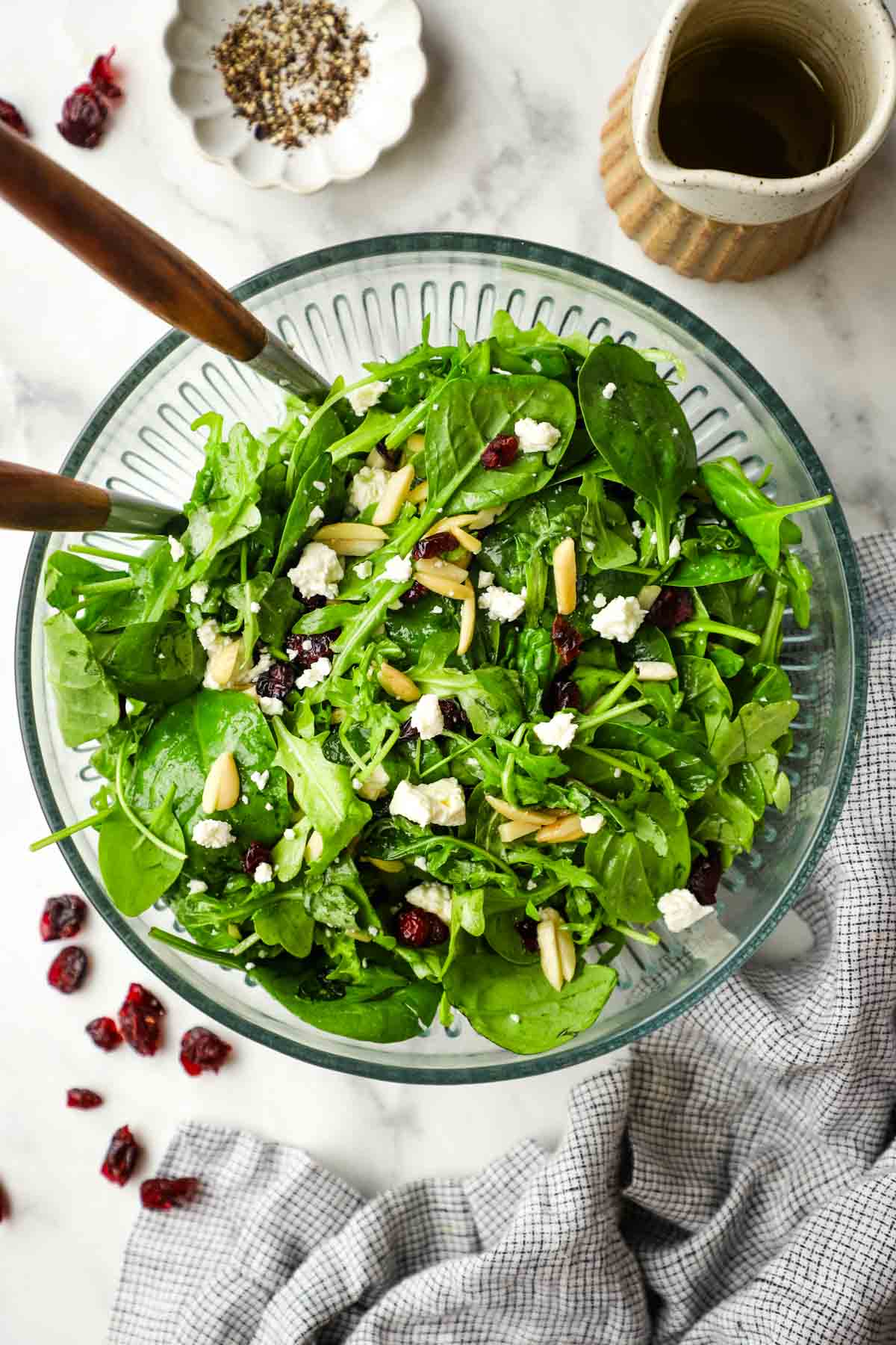 A serving bowl of spinach arugula salad topped with almonds, cranberries, and feta.
