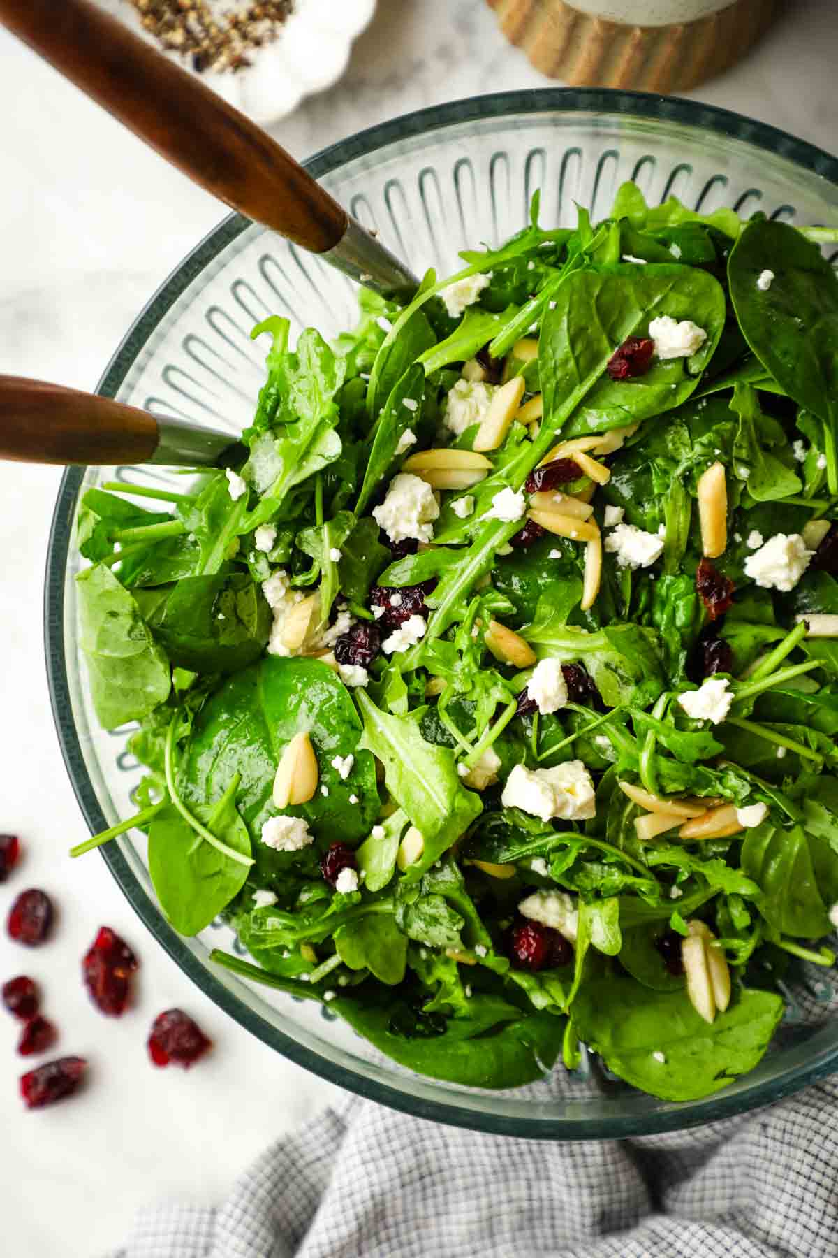 Spinach and arugula Salad in a serving bowl with serving utensils.