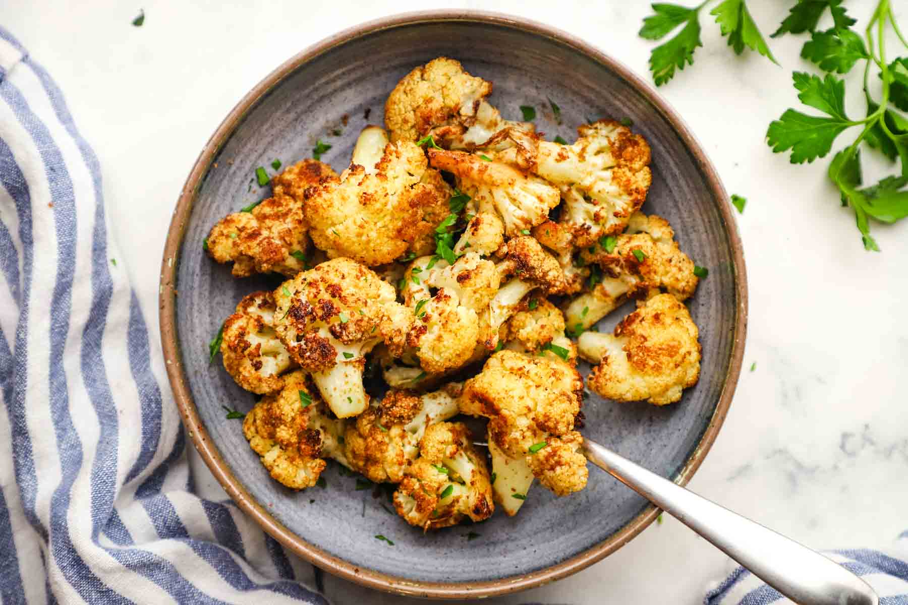 Crispy roasted cauliflower bites garnished with parsley in a bowl.