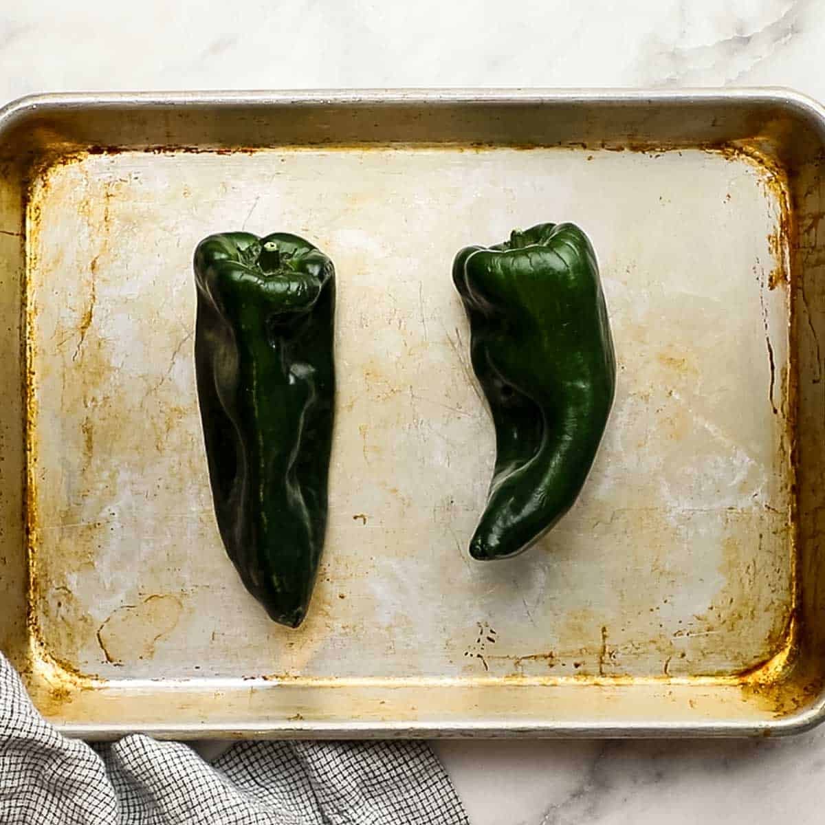Top-down of poblano peppers on a baking sheet, ready to be placed in the oven.