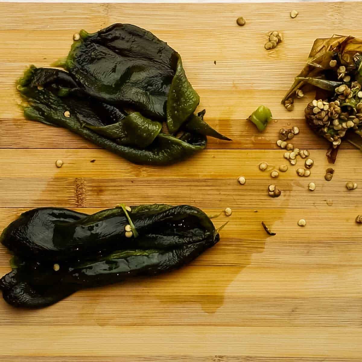 Two poblano peppers on a wood cutting board that have been skinned, and de-seeded