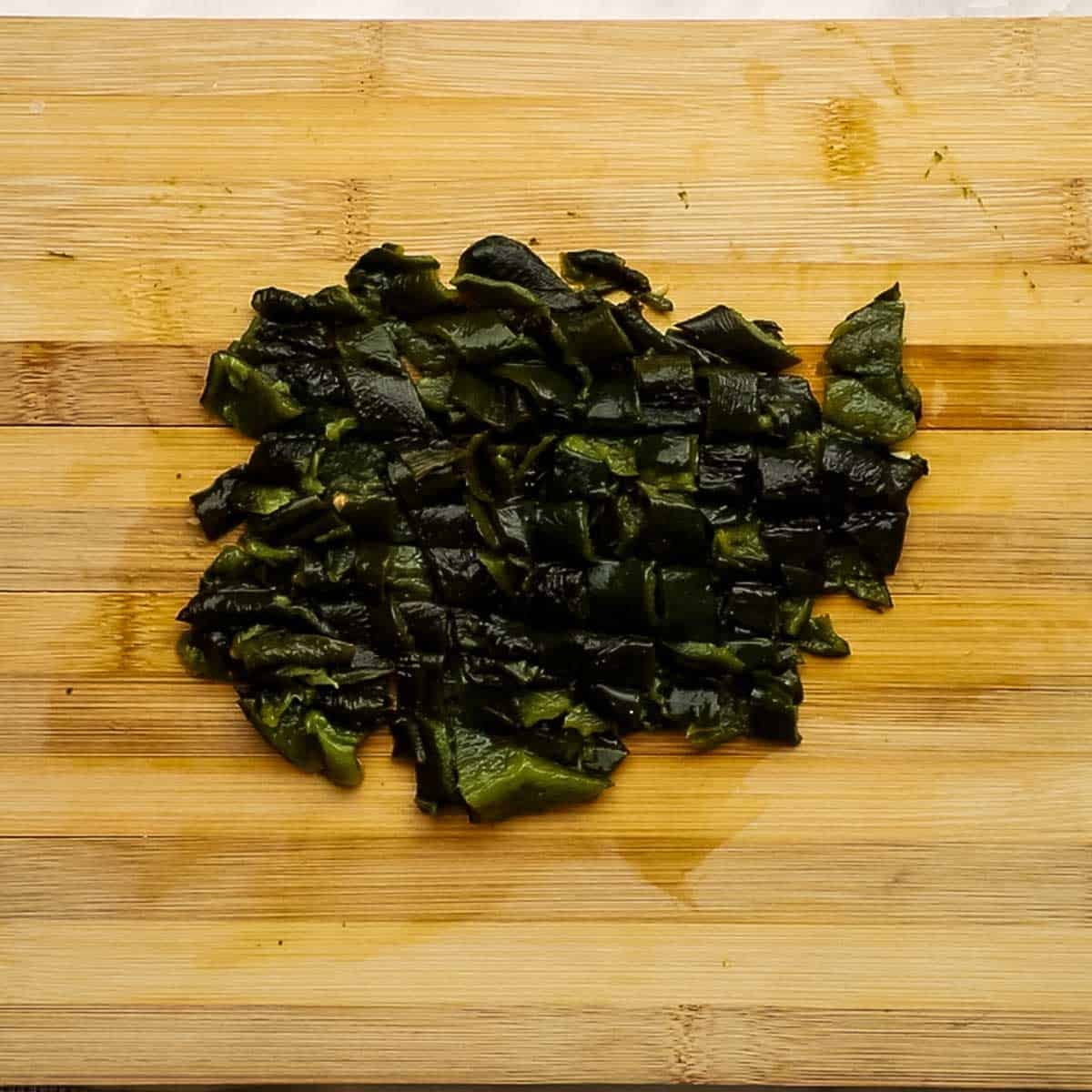 Two poblano peppers on a wooden cutting board that have been diced. 