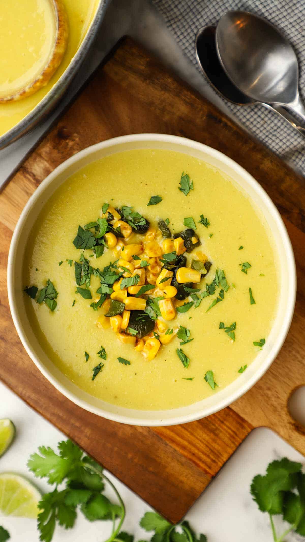 A close-up of poblano corn potato soup in a bowl on top of a wooden cutting board. 