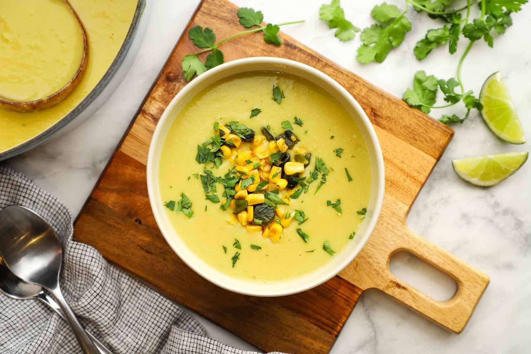 A bowl of creamy soup granished with corn, chopped poblano and cilantro.