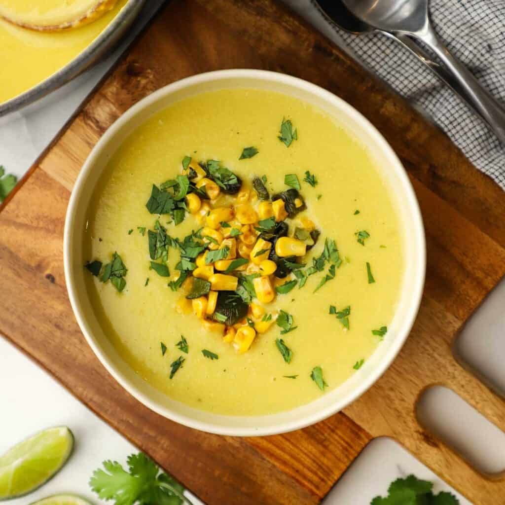 A bowl of roasted poblano corn and potato soup garnished with chopped corn, poblanos and cilantro.
