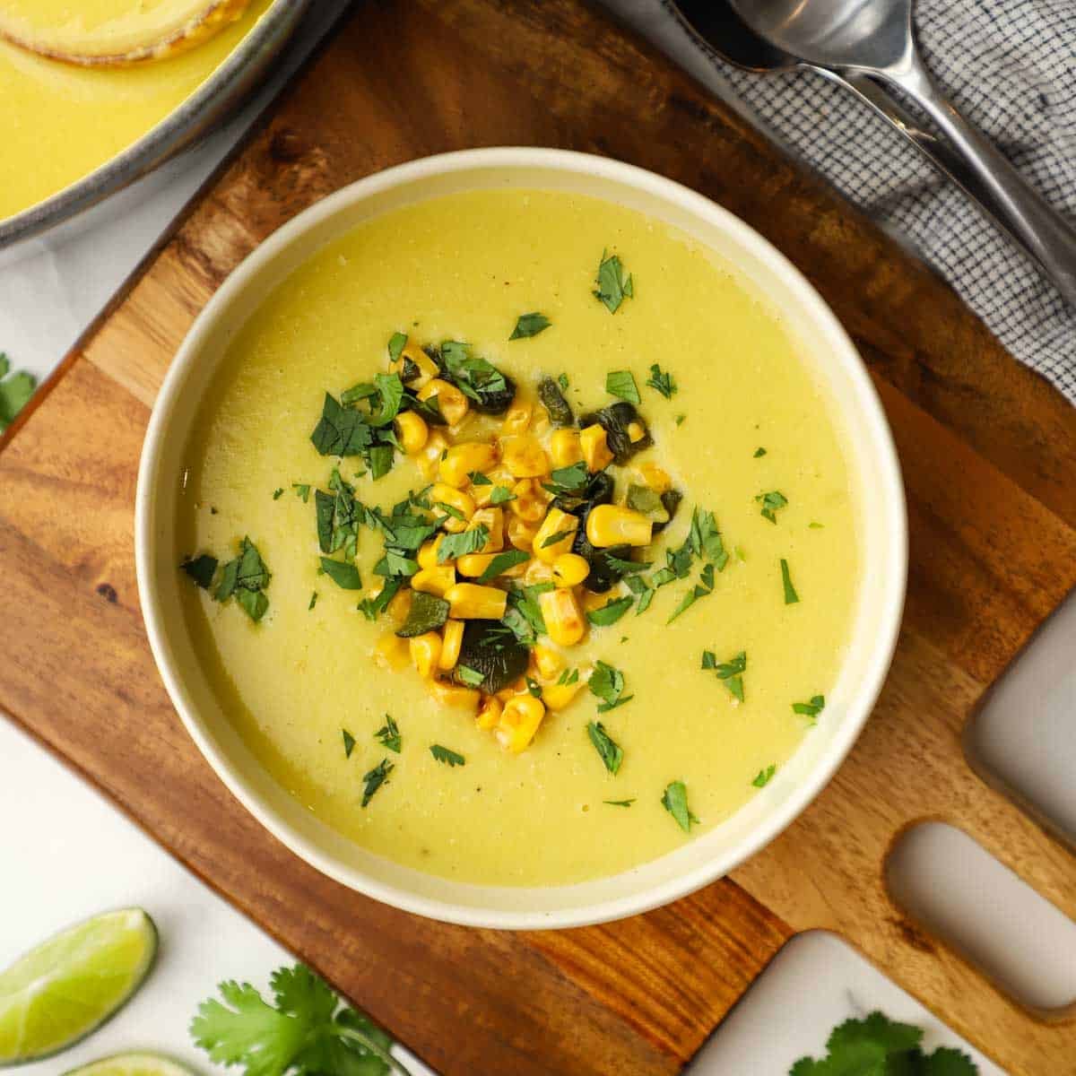 A bowl of roasted poblano corn and potato soup garnished with chopped corn, poblanos and cilantro.