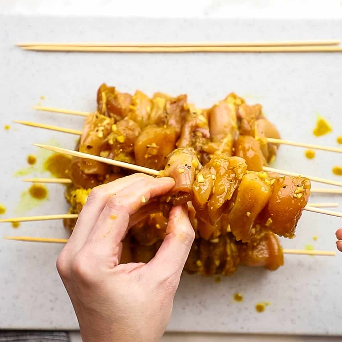 Chicken skewers being threaded onto bamboo skewers. 
