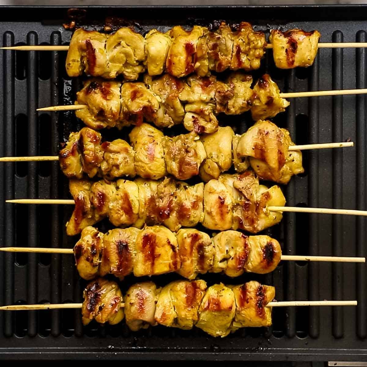 Chicken skewers threaded onto bamboo sticks are being grilled. 
