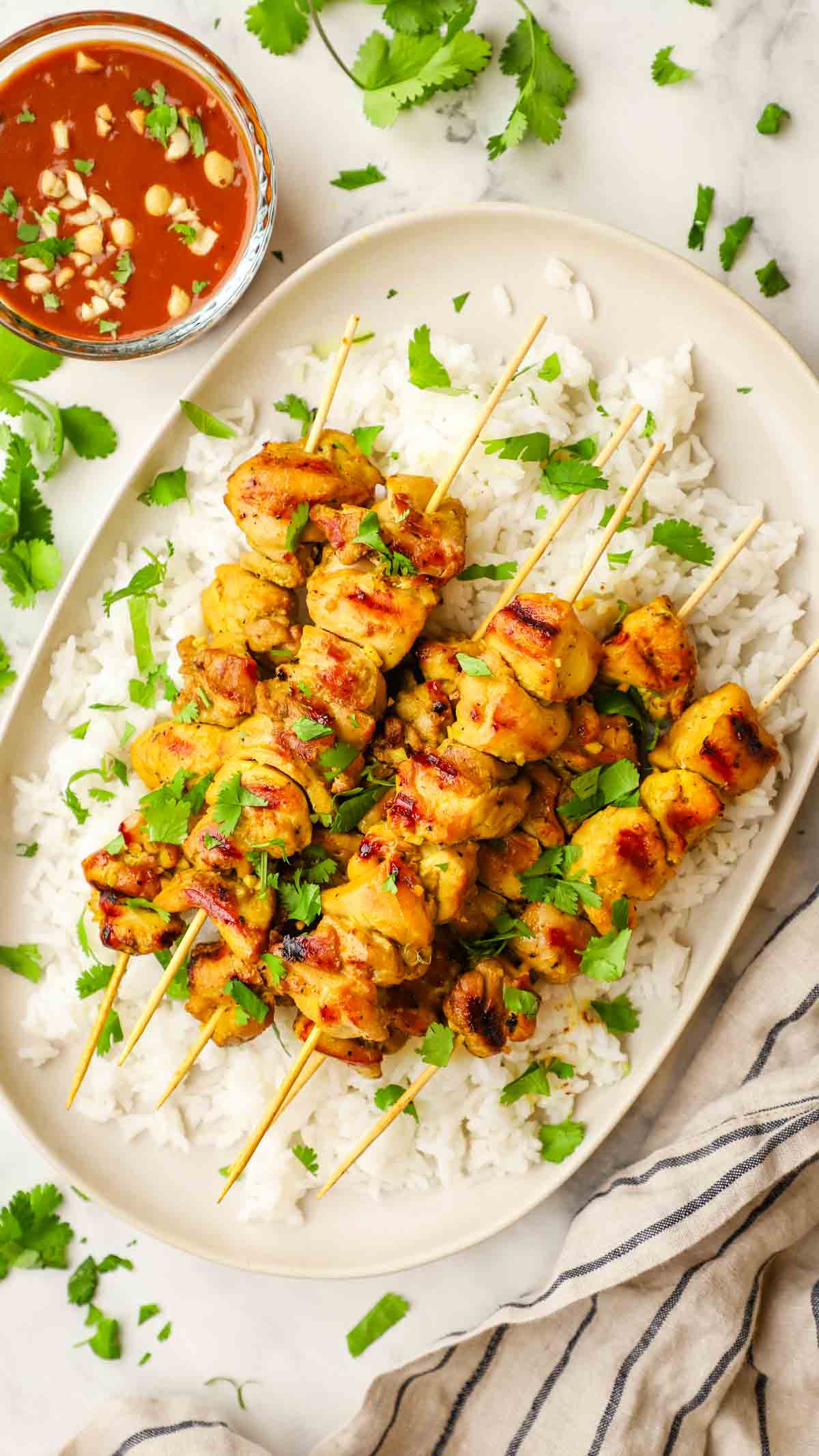 Grilled chicken skewers on a bed of rice with the wood skewers still intact, topped with cilantro.
