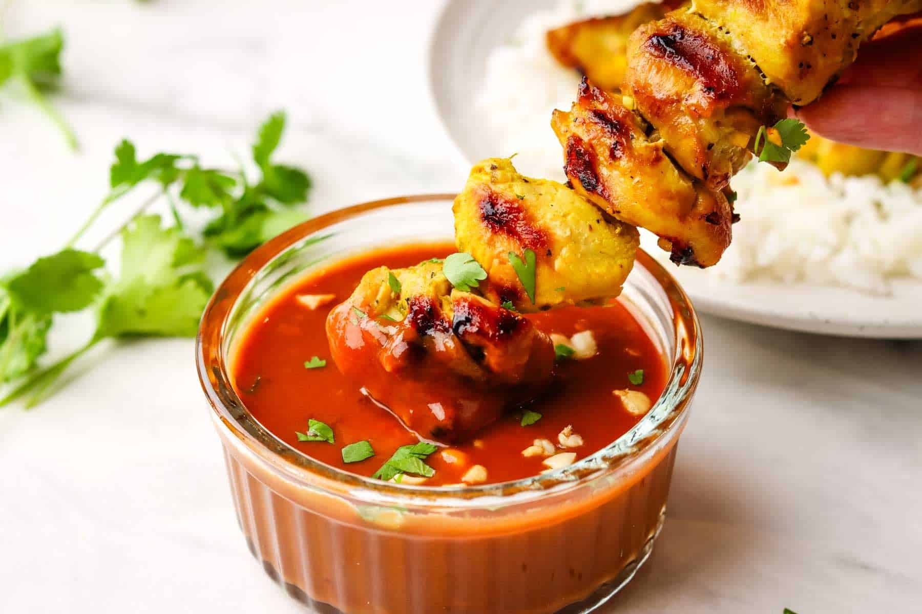 A chicken skewer being dipped into a bowl of peanut sauce.