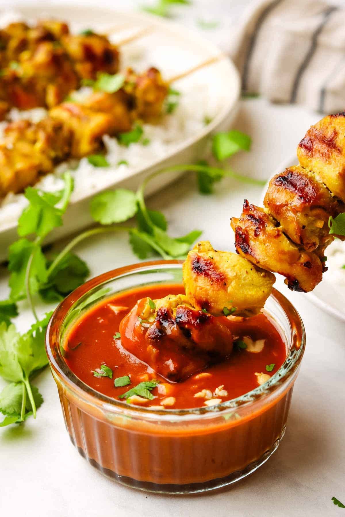 A chicken skewer being dipped into a bowl of peanut sauce.