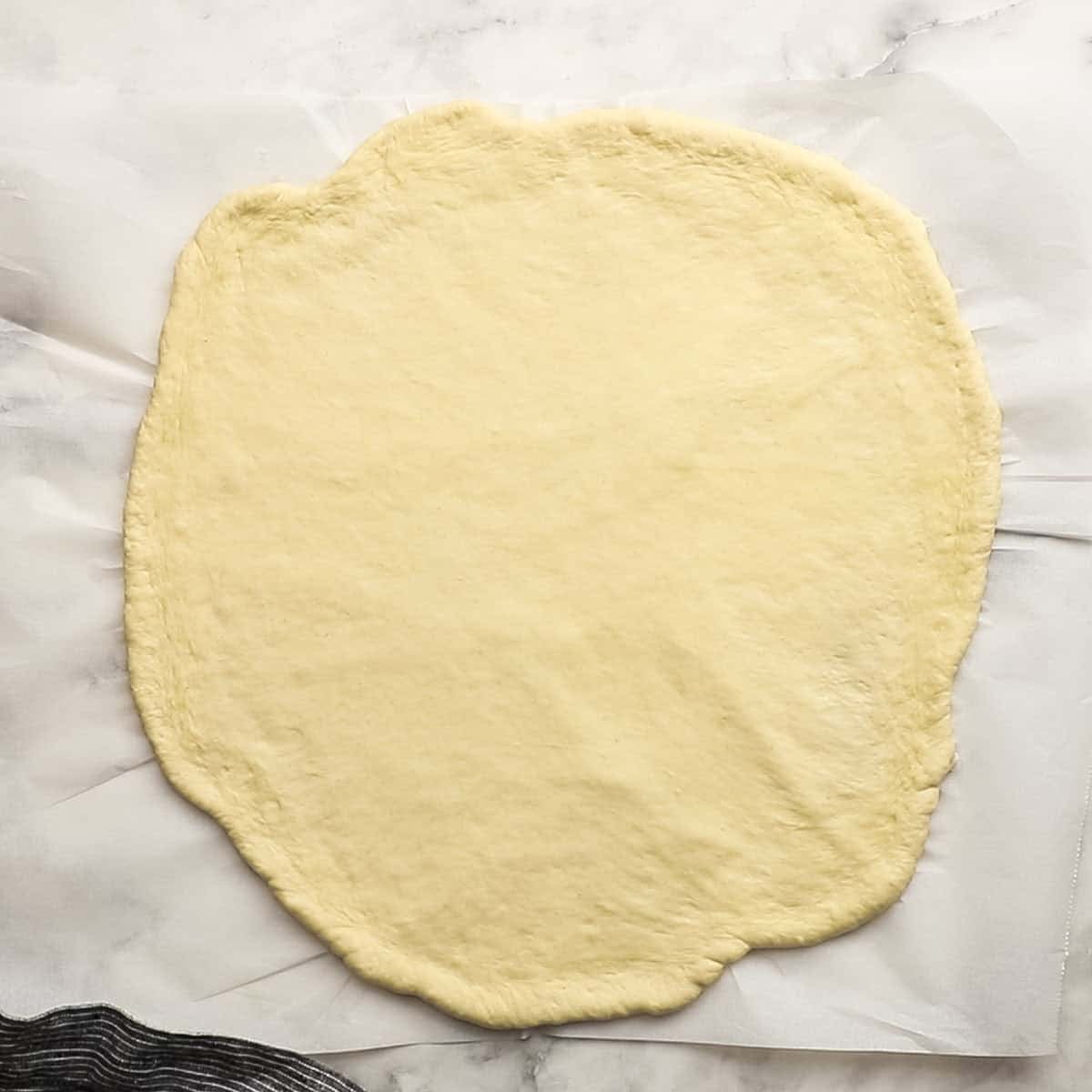A piece of parchment paper that has been sprinkled with semolina flour and has had pizza dough rolled out on it.