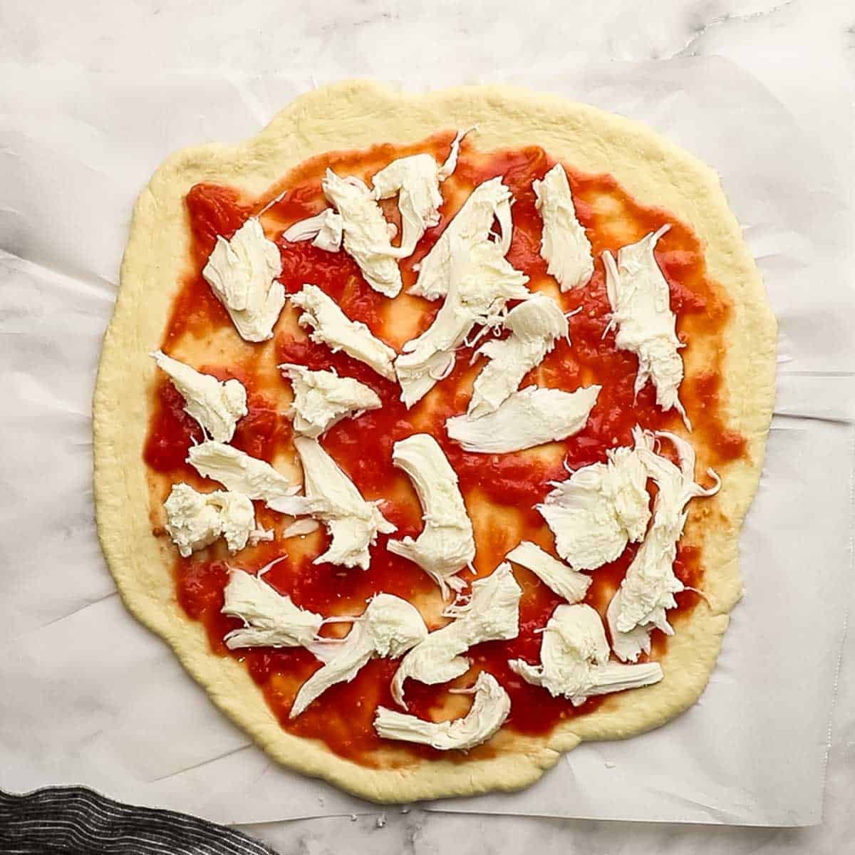 Fresh mozzeralla topped on pizza dough and homemade sauce, ready for the oven.