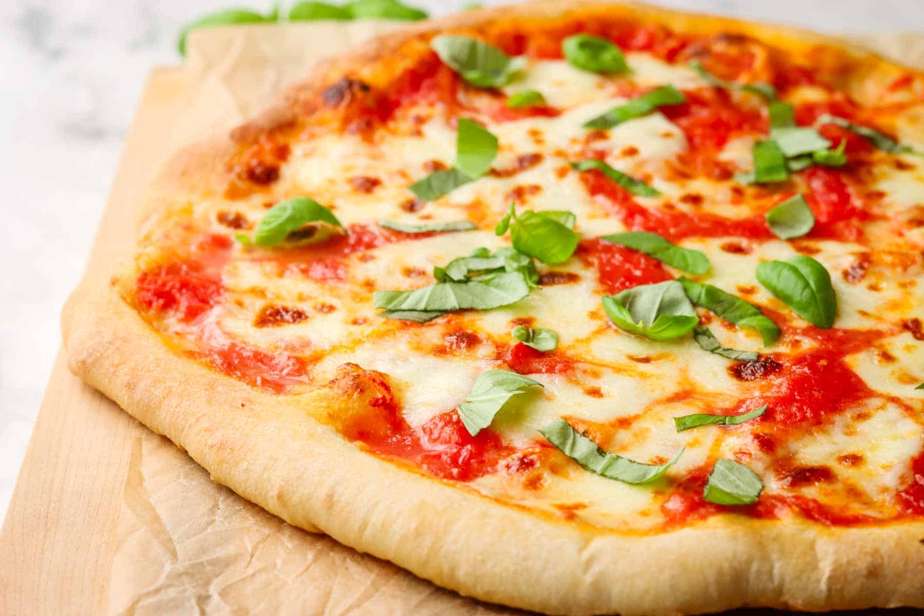 An unsliced margherita pizza on a wooden cutting board.