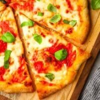 A slice of margherita pizza on a wooden cutting board.