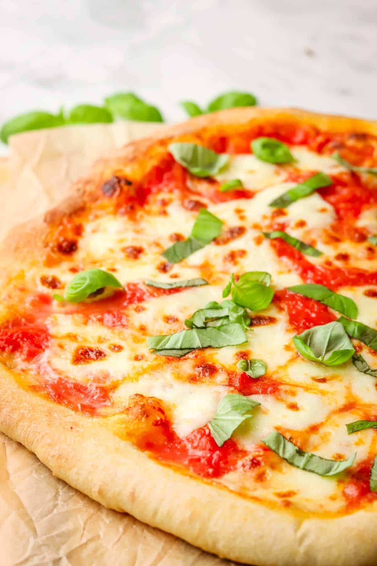 Side view of a margherita pizza with fresh basil on top, sitting on a wooden cutting board.