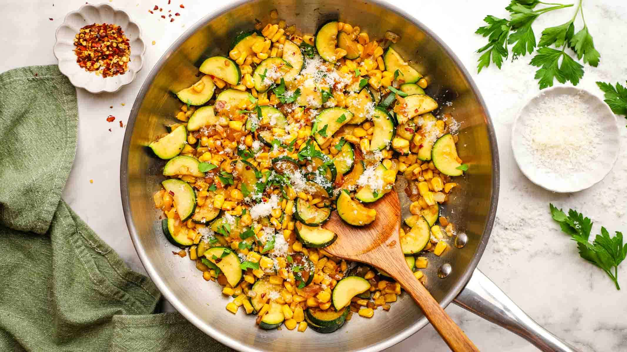 A pan of sauteed corn and zucchini garnished with Parmesan and chopped herbs.