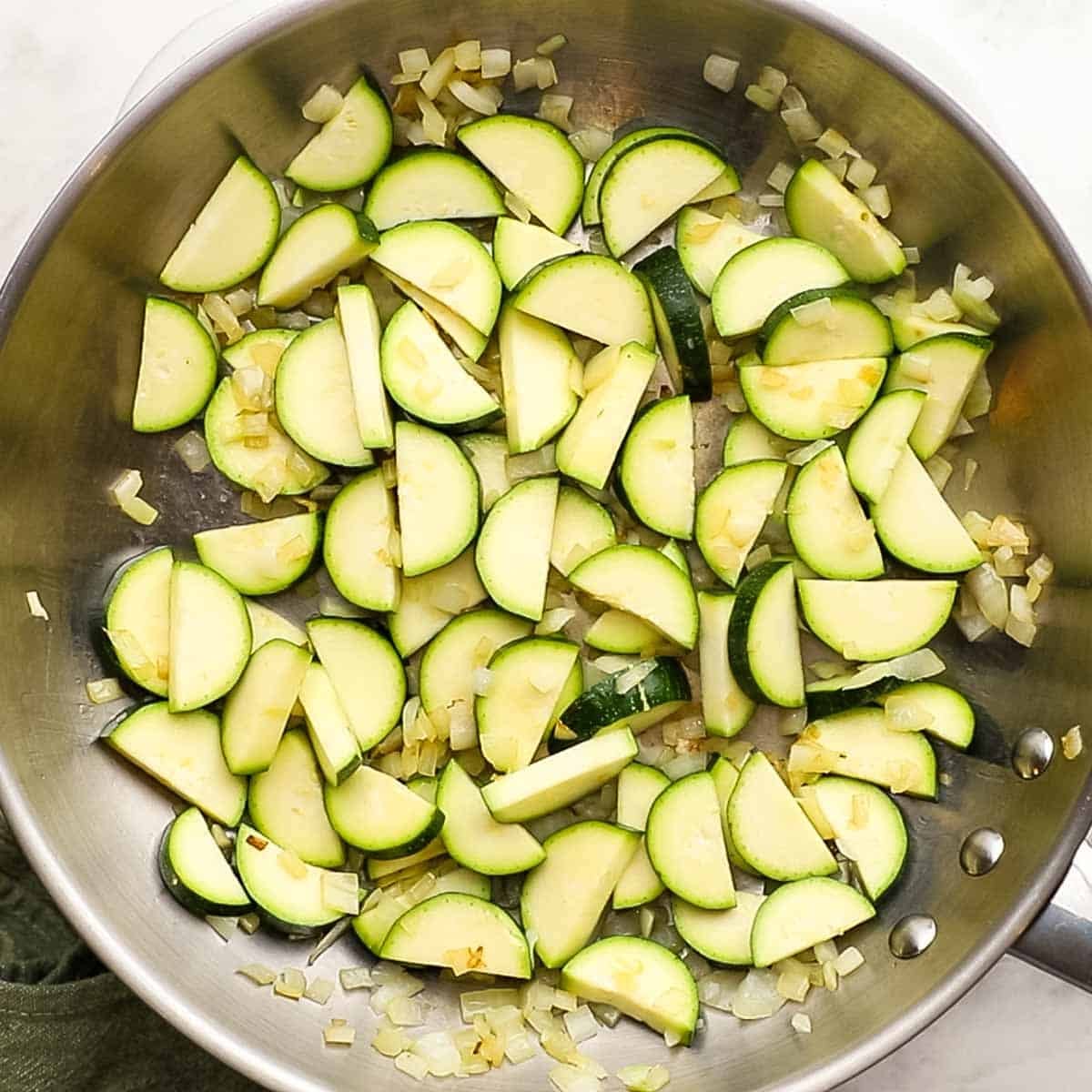 Zucchini in a skillet being sauted that has had added garlic and onion to it. 