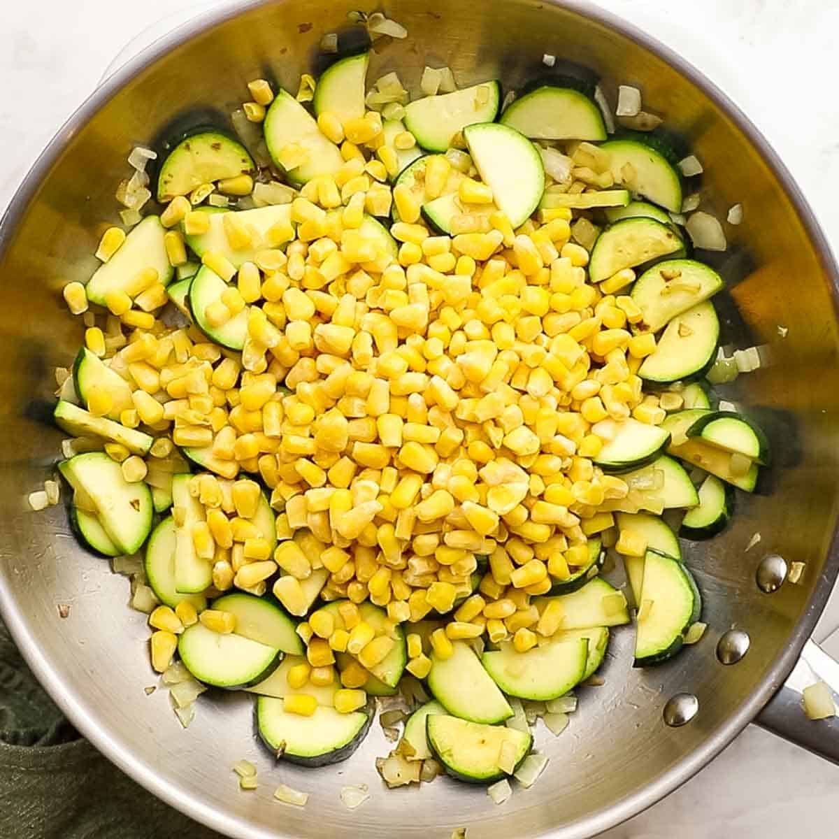 Sauted zucchini in a skillet that has had sweet corn added to it with garlic and onion. 