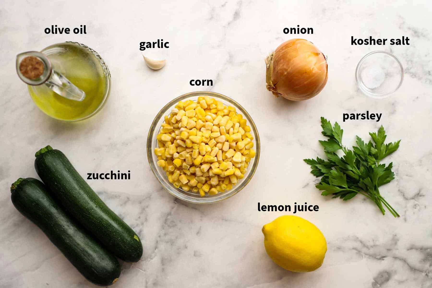 Top down views of ingredients for sauteed corn and zucchini that include white onion, salt, olive oil, garlic, parsley, zucchini, lemon juice, and corn in a bowl. 