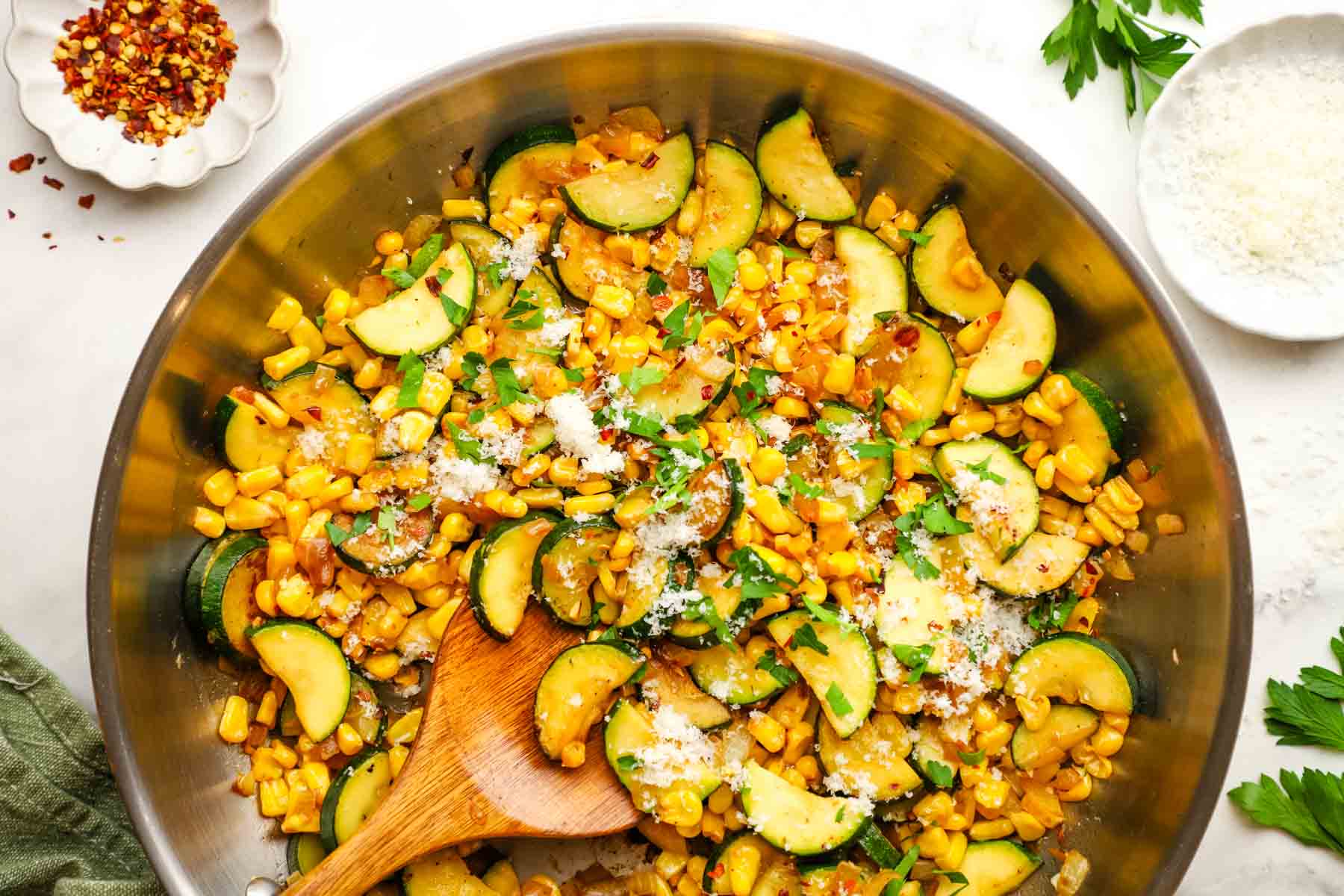 A pan of sauteed corn and zucchini garnished with Parmesan and chopped herbs.