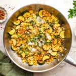 A pan of sauteed corn and zucchini garnished with Parmesan and chopped herbs.