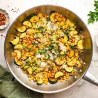 A pan of sauteed corn and zucchini garnished with Parmesan and chopped herbs.