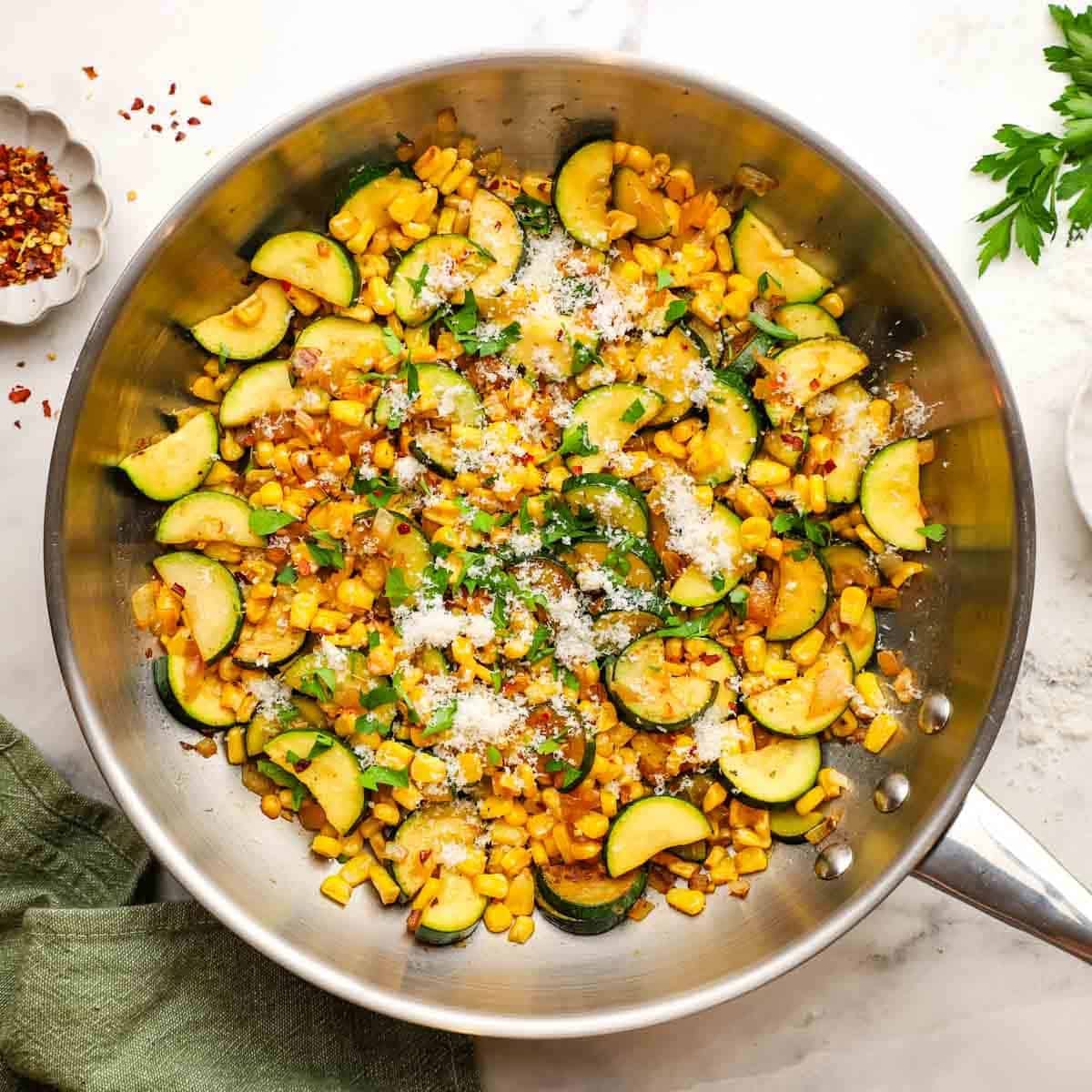 A pan of sauteed corn and zucchini garnished with Parmesan and chopped herbs.