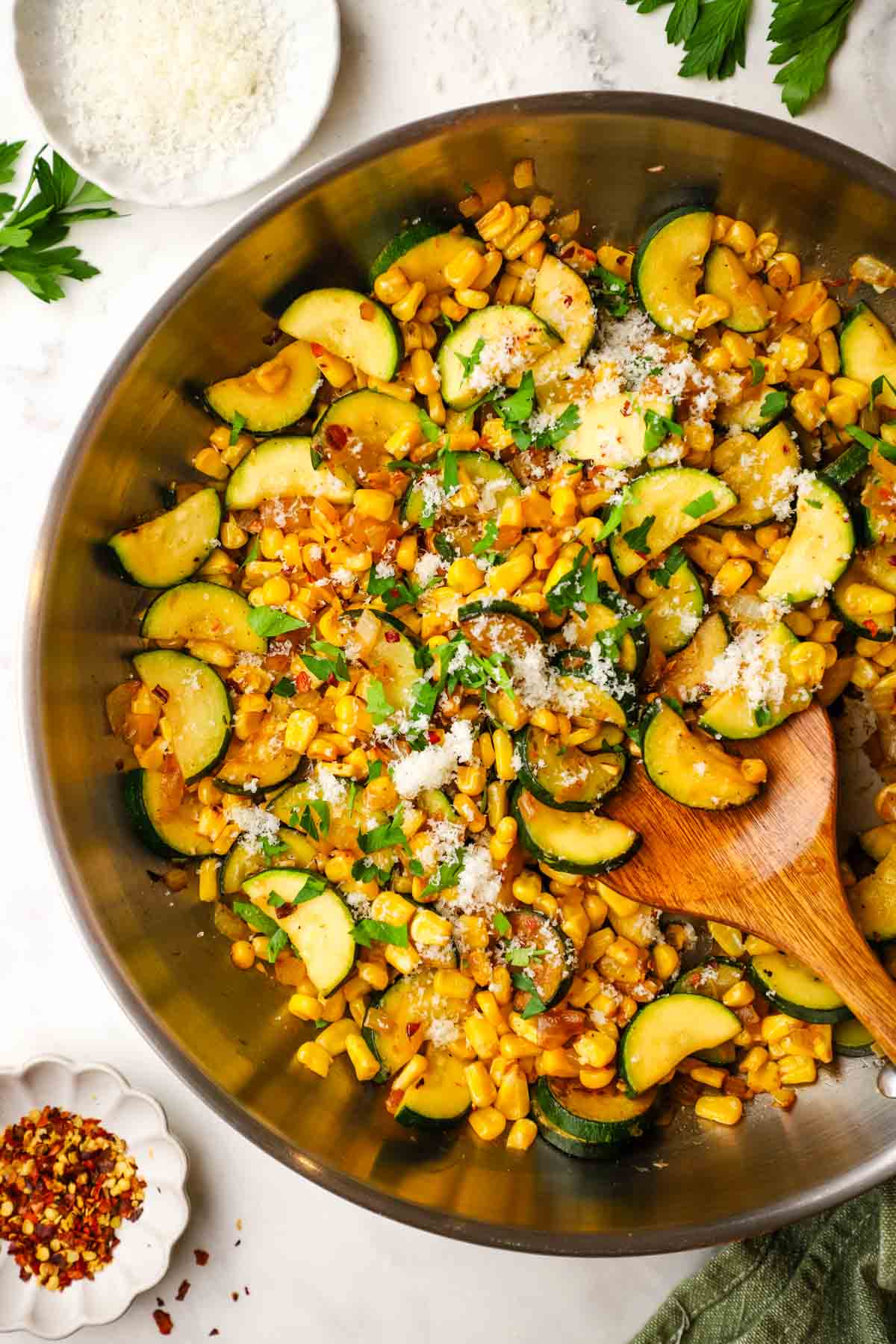 A pan of sauteed corn and zucchini garnished with Parmesan and chopped herbs.