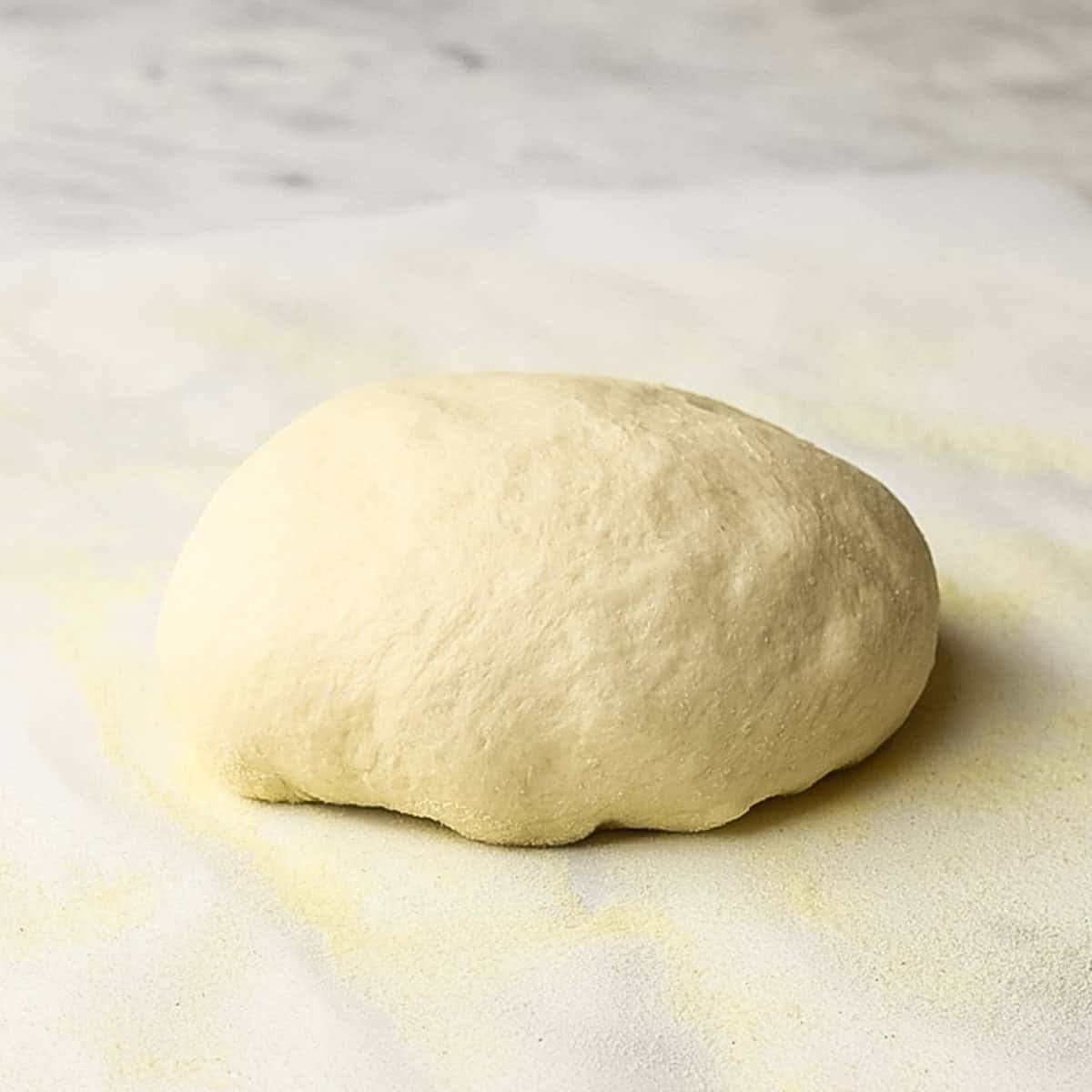 A side view of thin crust pizza dough resting on parchment paper.