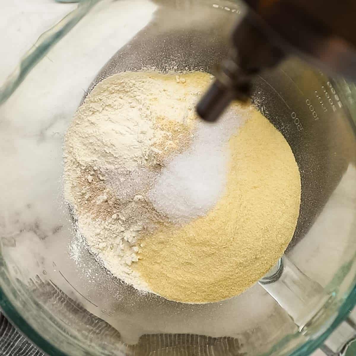 Top down view of flour, salt, sugar, and yeast in a glass bowl to be mixed for thin crust pizza dough