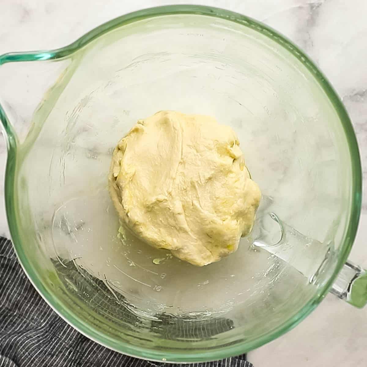 Top-down view of pizza dough that has been mixed with a dough hook and is now resting in a glass bowl.
