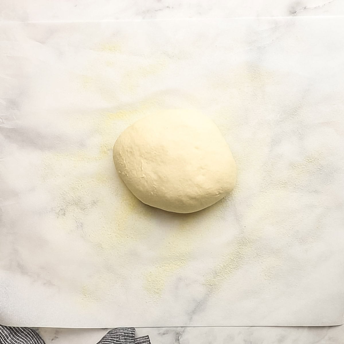 Top-down view of pizza dough on top of a little bit of semolina flour, prepped to be rolled out into a pizza crust.