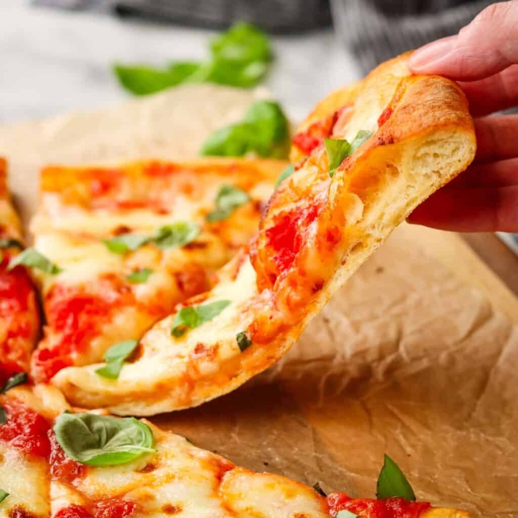 A slice of thin crust pizza being lifted off a sheet of parchment.