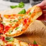 A slice of thin crust pizza being lifted off a sheet of parchment.