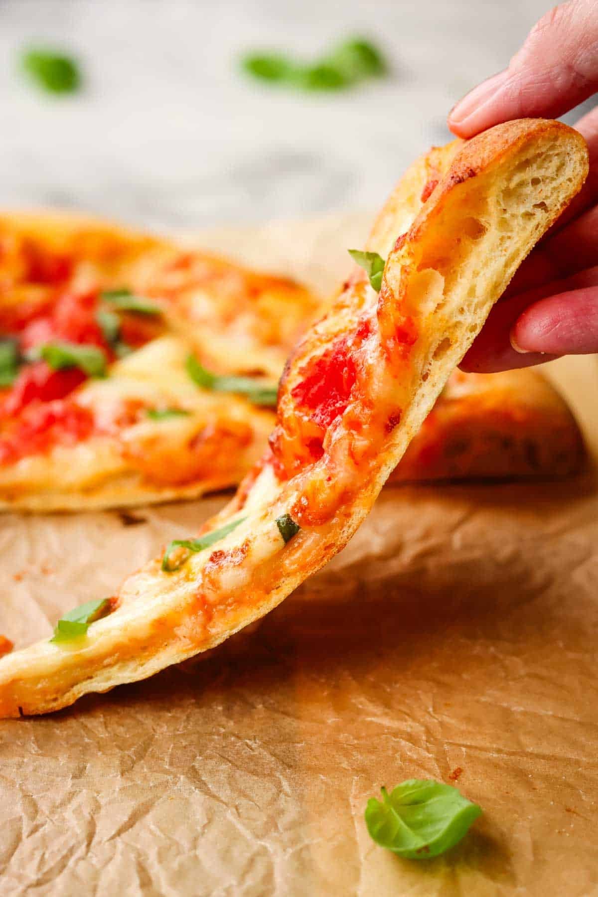 A slice of thin crust pizza being lifted off a sheet of parchment.