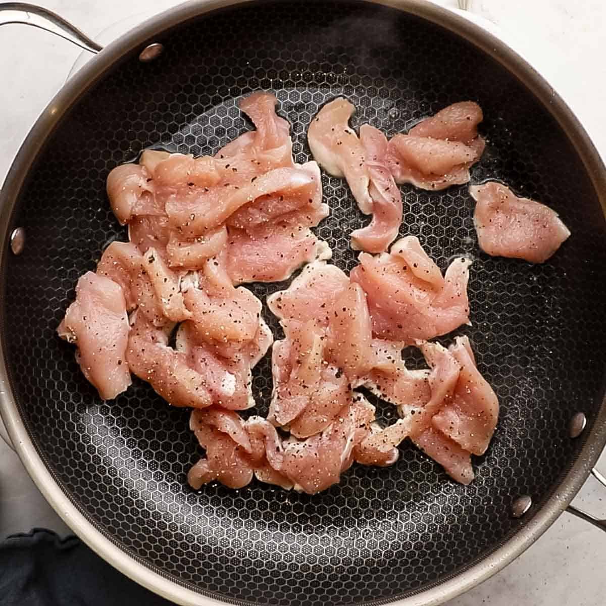 Top-down view of chicken breast that has been sliced and placed in  a skillet with olive oil.