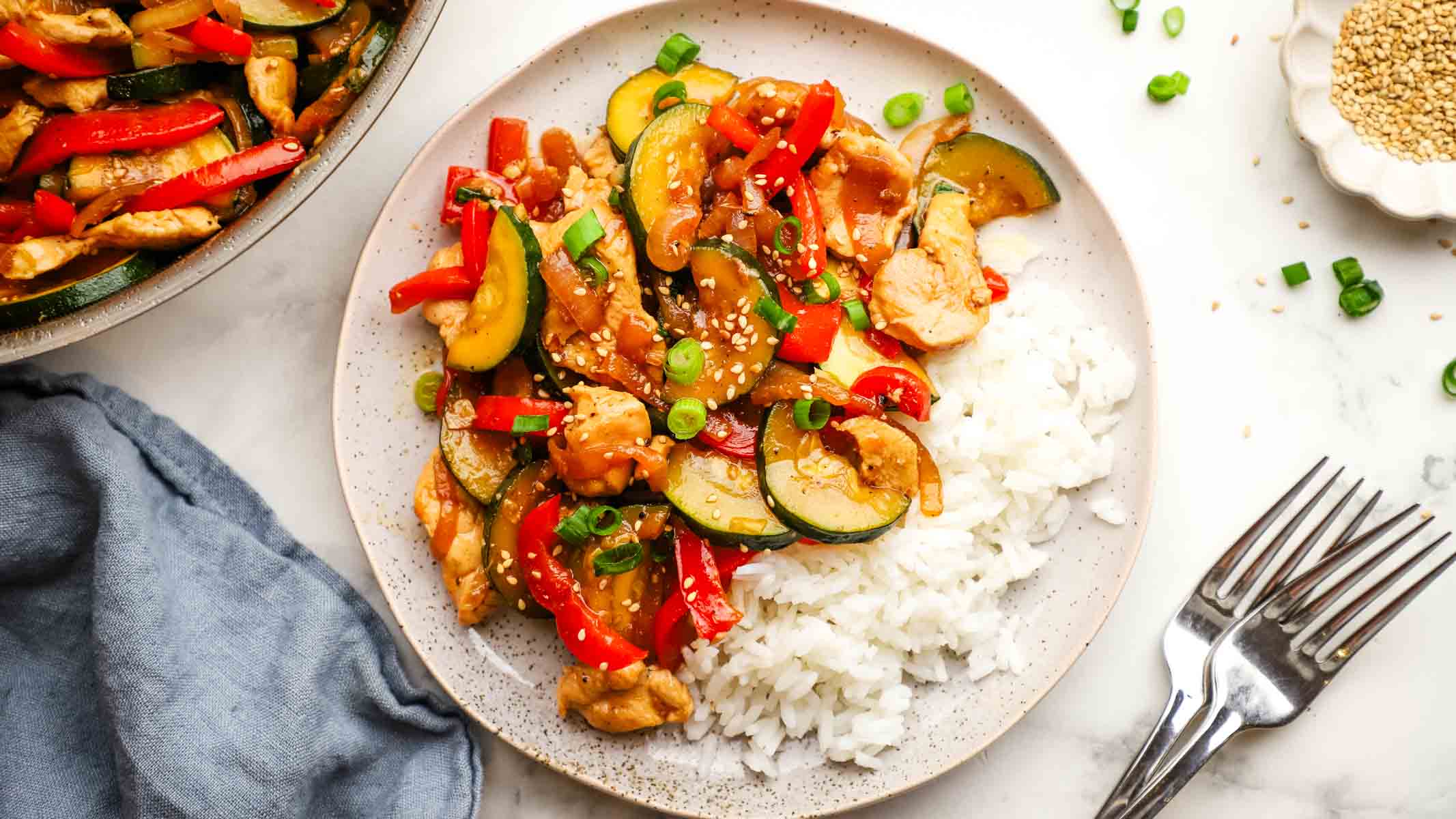 A plate of zucchini chicken stir fry on a bed of rice.