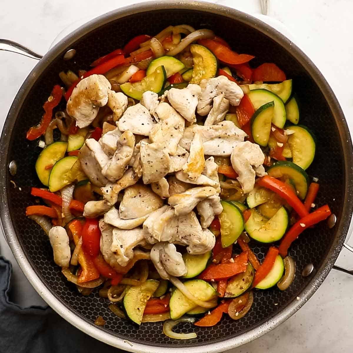 red pepper, zucchini, cooked chicken and now garlic added to the stir fry pan to be cooked for Stir-fry.