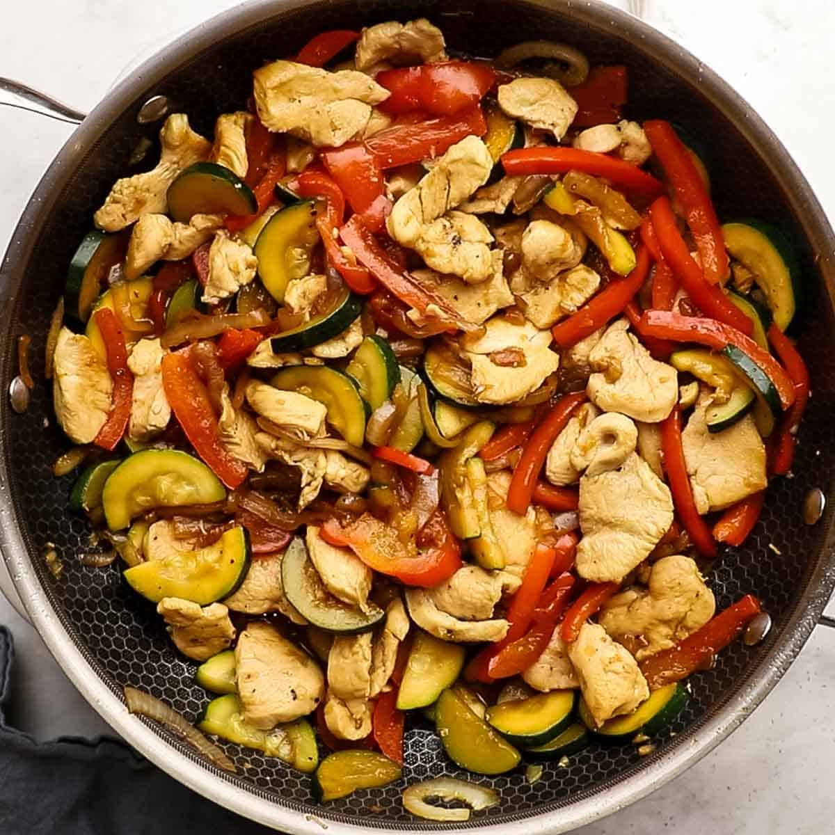 stir fry ingredients in the stir fry pan that include garlic, cooked chicken, bell peppers, zucchini now coated in the sauce and topped with soy sauce to taste. 