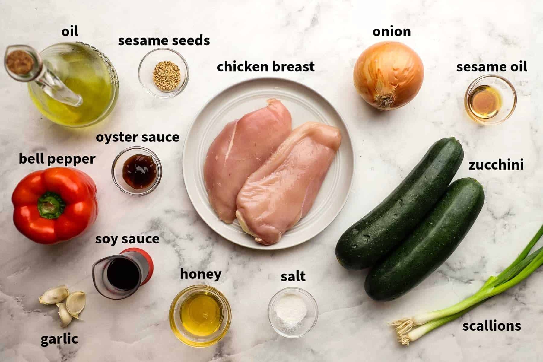 Top-down view of ingredients for zucchini- chicken stir fry that include chicken, zucchini, soy sauce, salt, honey, sesame seeds, and more.
