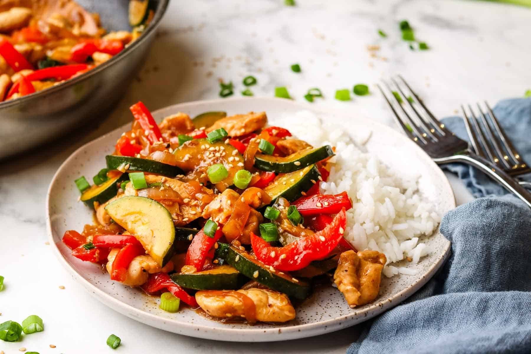 A plate of zucchini chicken stir fry on a bed of rice.
