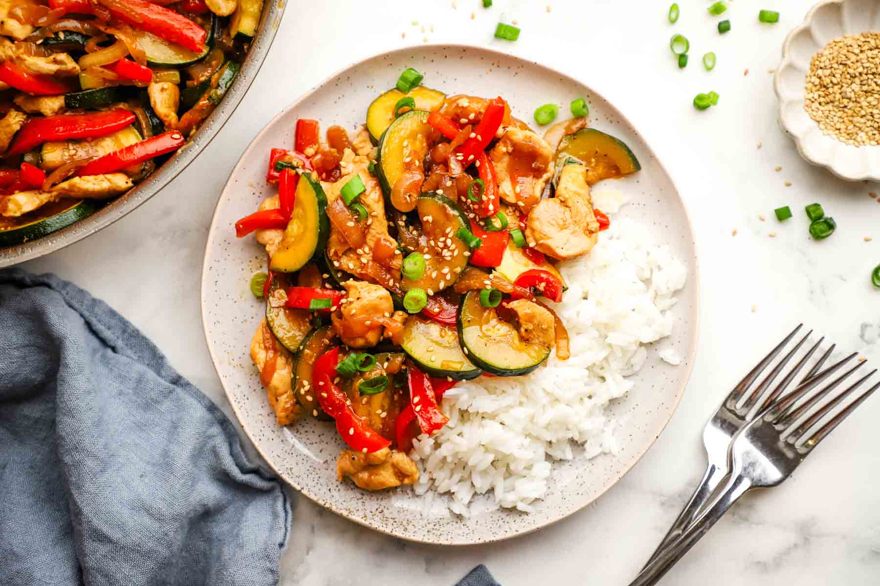 A plate of zucchini chicken stir fry on a bed of rice.