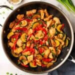 A pan of zucchini chicken stir fry with red bell peppers.