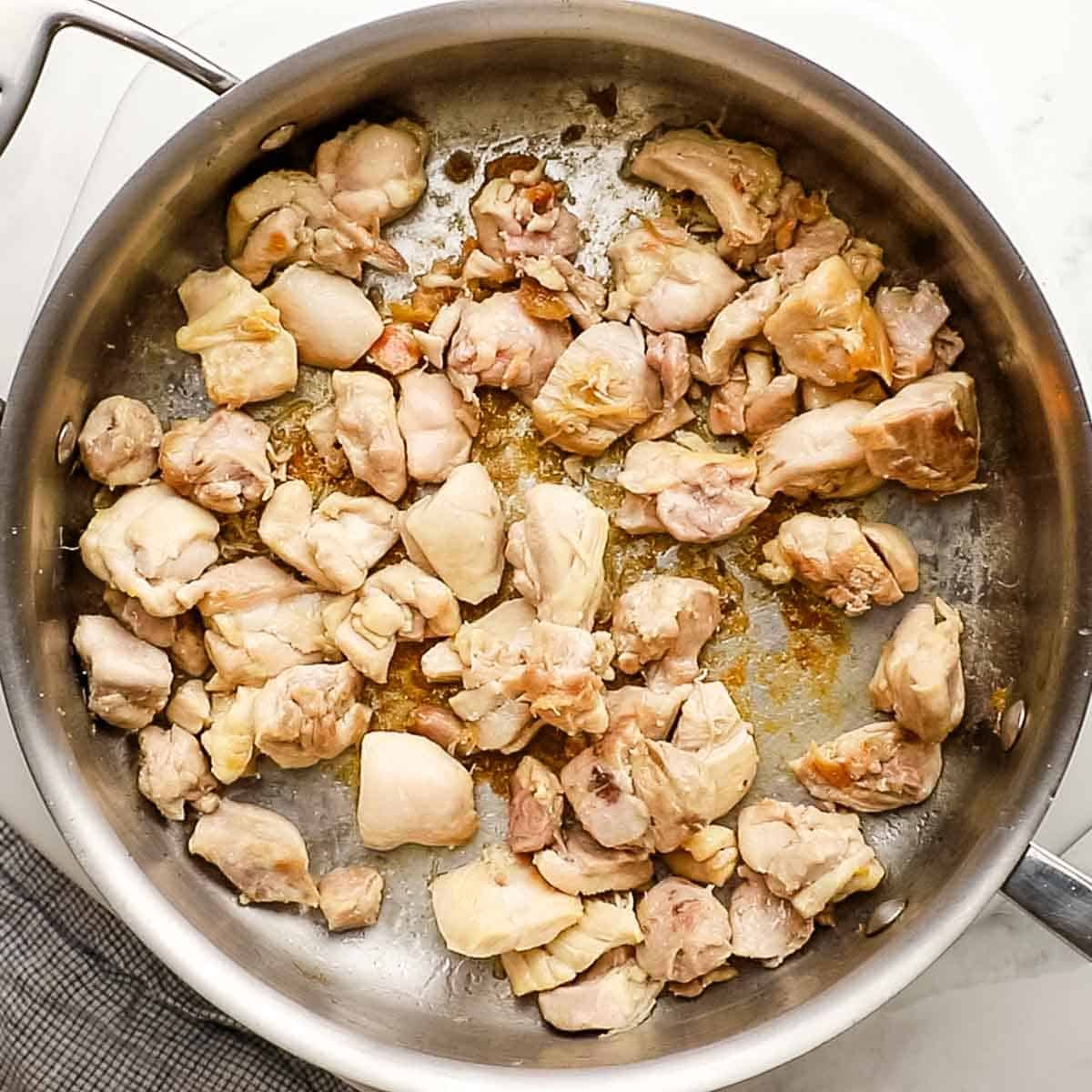Diced chicken thighs browning in a skillet for chicken and chickpea curry