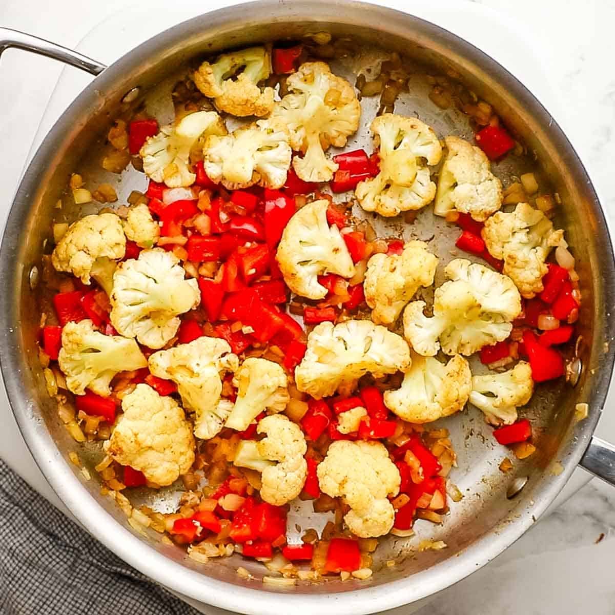 Cauliflower and red bell pepper added to the onion and garlic and cooking in the pan.
