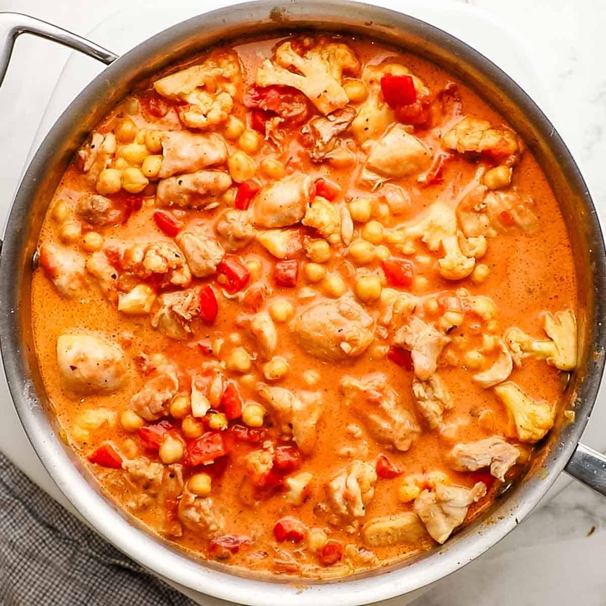 Fire-roasted tomatoes, chickpeas, reserved chicken, and coconut curry paste mixture added to the onion, garlic, and cauliflower mixture in the pan.
