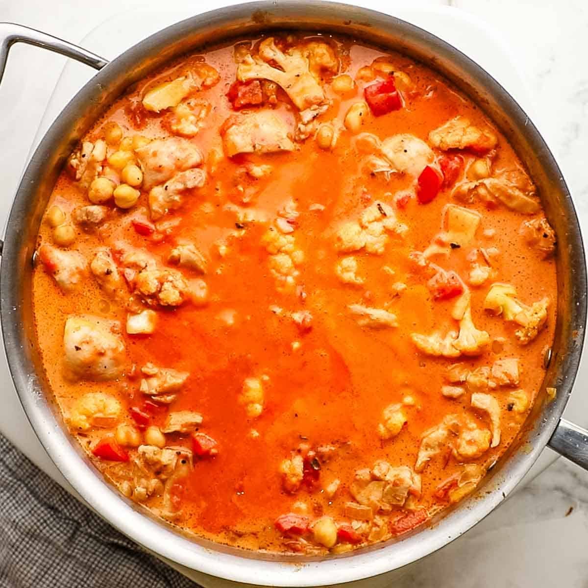Chicken, coconut mixture and cauliflower mixture all simmering in a pan for chicken and chickpea curry.