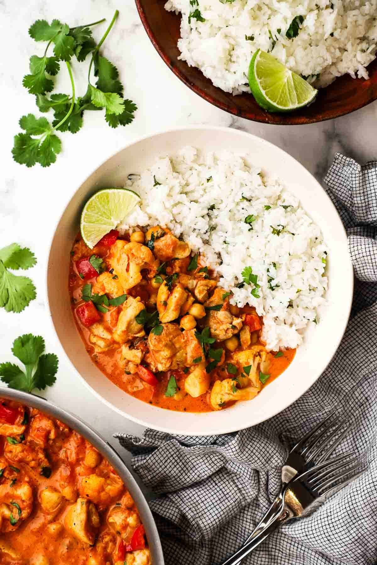 Chicken and chickpea curry served with a side of rice and garnished with a wedge of lime in a bowl.