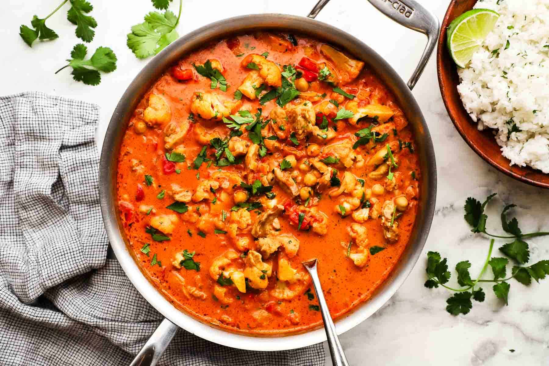 A pan of chickpea and chicken curry with a serving spoon in it.